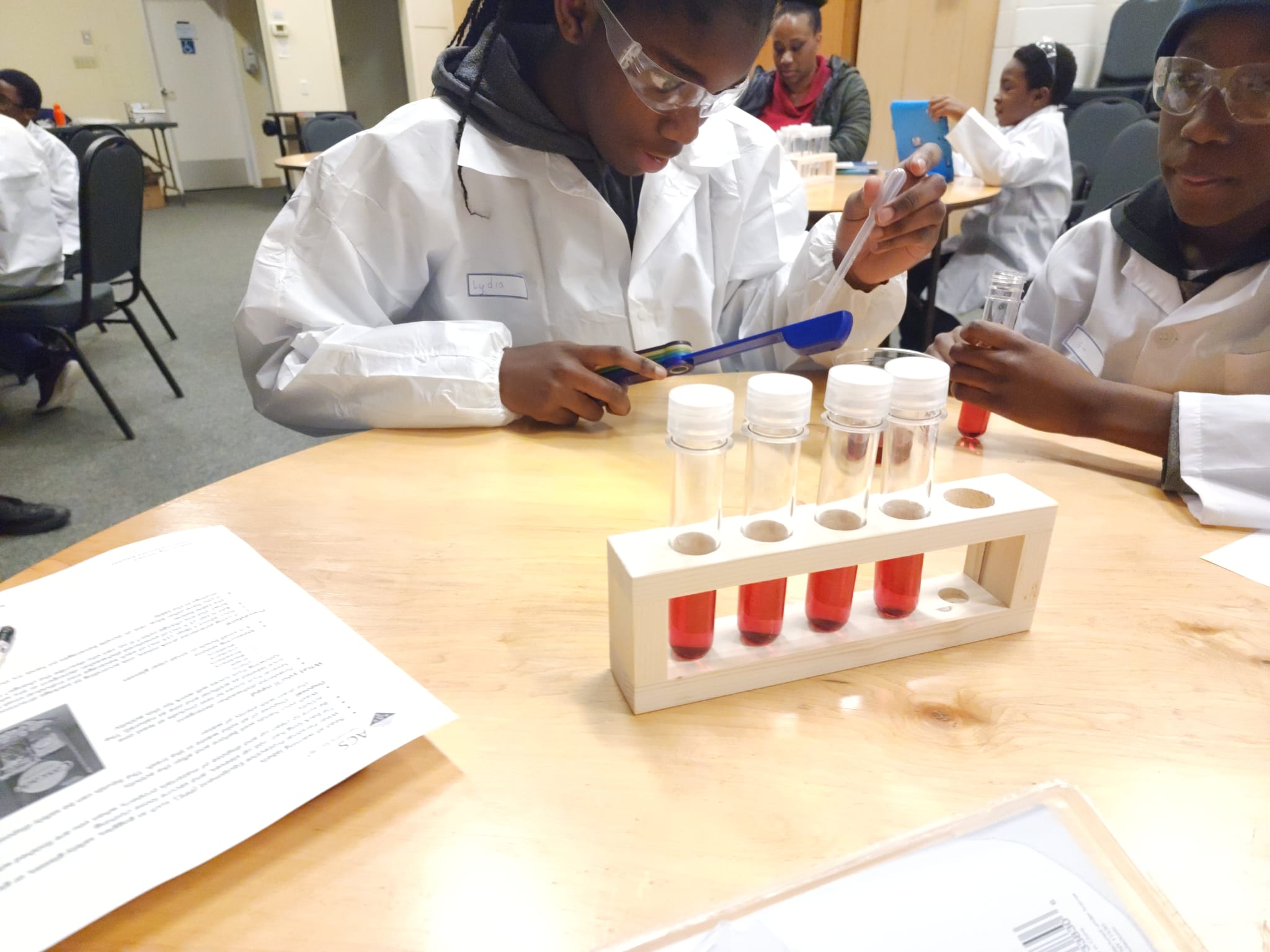 Participants in goggles use tubes and a dropper during a science activity