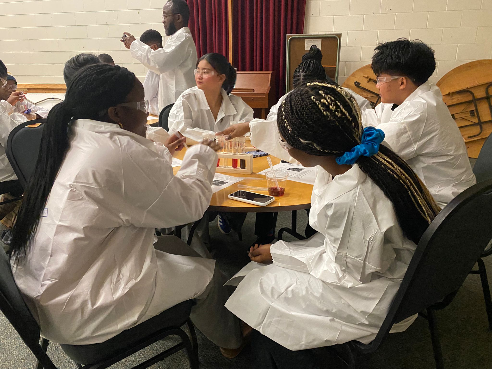 Participants wearing goggles explore test-tube activities around a workshop table